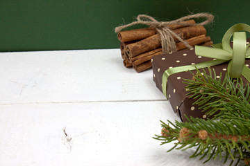 Christmas gift with decoration with pine branches cinnamon and green ribbon on white wood background