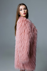 portrait of beautiful young woman in pink fur coat posing in studio