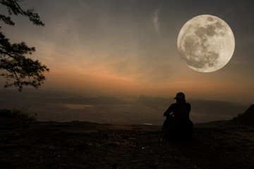 beautiful scenery - woman sitting serenely of the cliff and looking at the valley and mountains with moon
