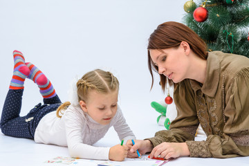 Mum with a small daughter are preparing toys and dress up a Christmas tree on a white background