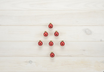 Fototapeta na wymiar Bolas decorativas de navidad de color rojo dibujando un árbol sobre fondo de madera blanca