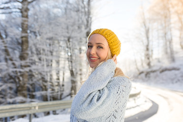 Winter portrait of a young smiling woman in a yellow hat on a ba