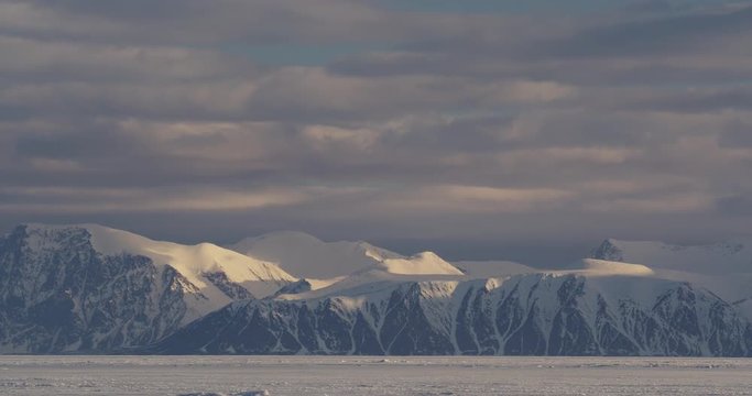 Time lapse - Snowy mountains by sea ice with clouds racing above