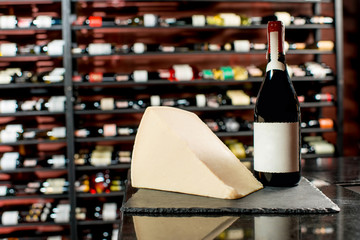 A bottle of wine with a piece of parmegiano cheese on the black board in supermarket or restaurant . Bottle with empty label to copy paste