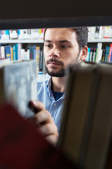 male college student taking book from shelf in library.