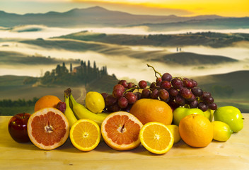 Obrazy na Szkle  owoce na drewnianym stole i toskański krajobraz o wschodzie słońca