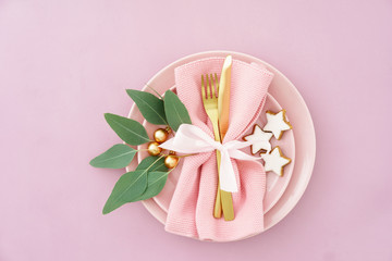 Fototapeta na wymiar Christmas place setting in pink with golden silverware, eucalyptus and cinnamon stars