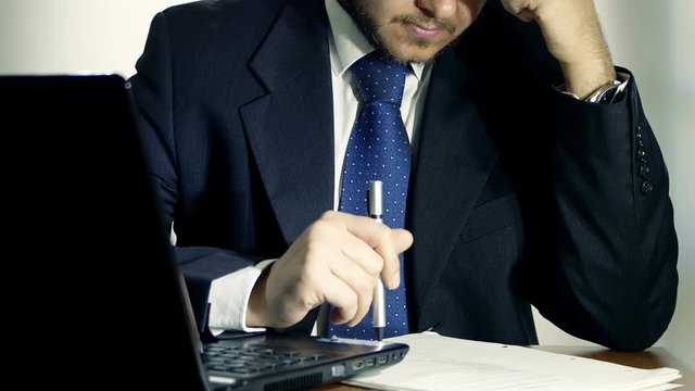 tired businessman working on some documents with laptop in foreground