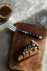 Slice of raw chocolate mousse cake  with cashew nuts, hazelnuts and dark chocolate glaze topping and hot coffee on a wooden and grey stone background. Vegan sugar, gluten, dairy free dessert. 