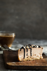 Slice of raw chocolate mousse cake with cashew, hazelnuts and dark chocolate glaze topping and coffee on a wooden and grey background. Vegan sugar, gluten free dessert. Copy space
