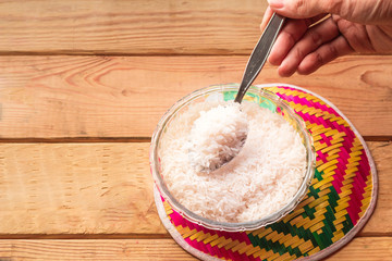 Hand holding Rice in bowl and colorful tray on wooden table.