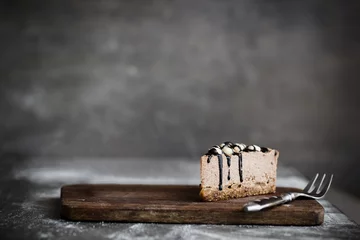 Gordijnen Slice of raw chocolate mousse cake with cashew, hazelnuts and dark chocolate glaze topping and coffee on a wooden and grey background. Vegan sugar, gluten free dessert. Copy space © Iuliia