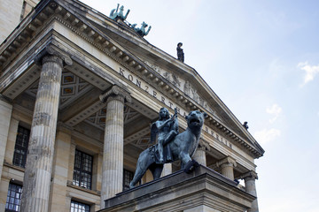 Obraz premium Winged musician young boy plays an instrument while riding lion statue in front of Konzerthaus Berlin. Classical building, opened in 1821, with ornate halls for orchestral concerts & chamber music.