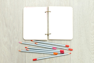 Opened blank notepad with colorful pencils on wooden table