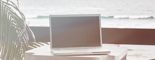 Computer on table outside on apartment balcony. Vacation workplace for laptop  in tropical resort for digital lifestyle blog, freelancer business, image with filter effect