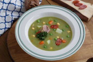Pea soup with smoked sausage on wooden background.