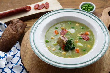 Pea soup with smoked sausage on wooden background.