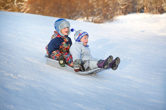 Two joyful child sledding down the hills in a winter day.