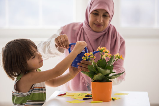Arabic mother with little son in living room watering flowers