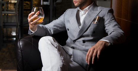 Male model in a suit, sitting on a leather armchair holding whiskey