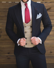 Male model in a three part suit posing in front of a wooden wall