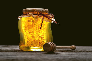 jar of honey with honeycomb with wooden dipper on wooden table
