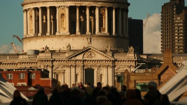 Telephoto shot of anonymous crowds walking past the famous St Pauls Cathedral in London, England, UK on a sunny day
