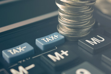stack of coins on calculator near tax sign