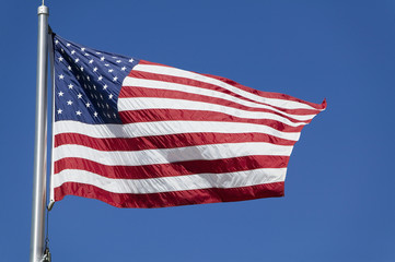 Fototapeta premium American flag waves in the wind against a blue sky