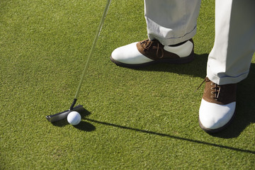 Closeup of legs with golf club and ball on grass