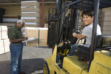 Portrait of a male worker driving forktruck and senior man writing on the clipboard