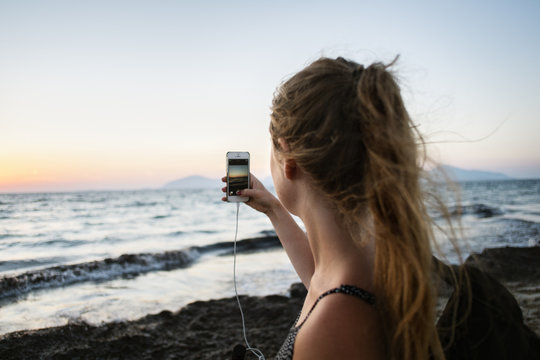 Greece, Kalymnos, Young woman photographing sunset sky with smart phone