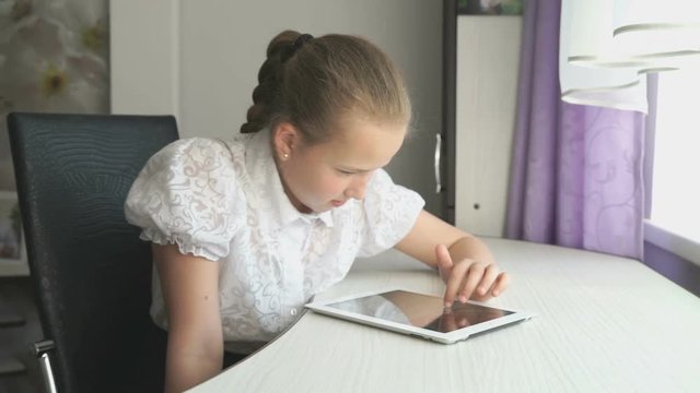 Teenager girl smiles while uses a digital tablet computer at the desk at home