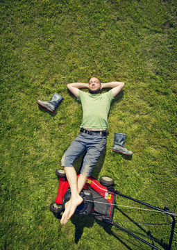 Finland, Man lying on grass with feet up on lawn mover in summer