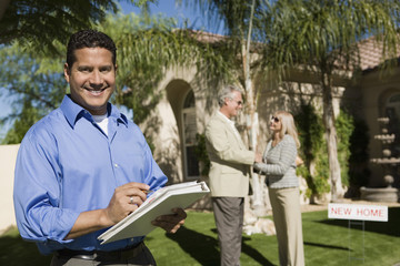 Portrait of happy real state agent holding file folder with couple in background