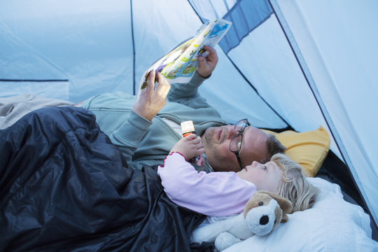 Sweden, Father and daughter (4-5) reading comic book in tent