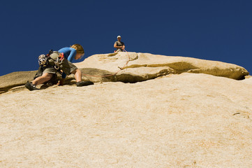 Low angle view of man assisting friend climbing rock against clear blue sky