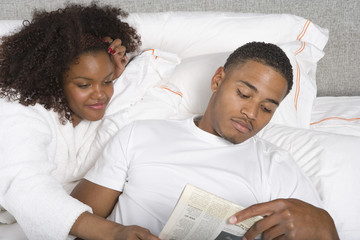 Young African American couple reading newspaper in bed