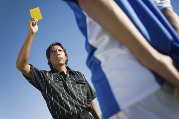 Low angle view of a referee showing a yellow card that indicates a late tackle