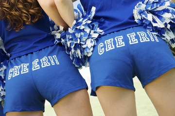 Closeup rear view midsection of two cheerleaders holding pom poms