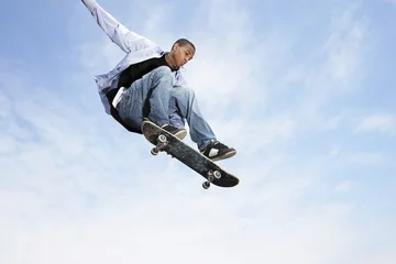Tuinposter Low angle view of young man on skateboard in midair against cloudy sky © moodboard