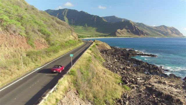 AERIAL: Couple In Red Convertible Car Driving Along The Beautiful Coastal Road