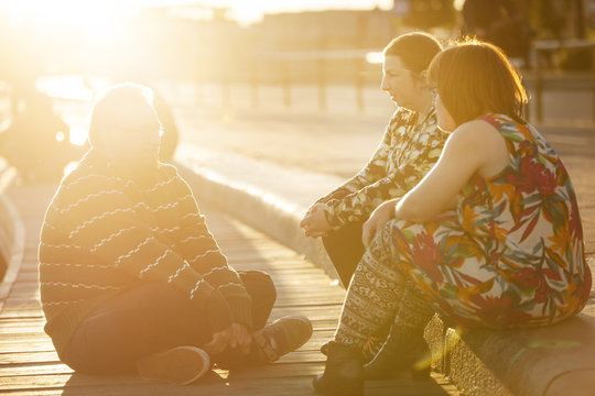 Sweden, Sodermanland, Stockholm, Sodermalm, Slussen, Woman with down syndrome sitting on promenade with friends at sunset