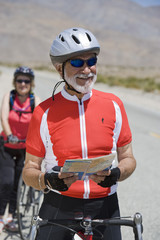 Happy senior male bicyclist holding map with woman in the background