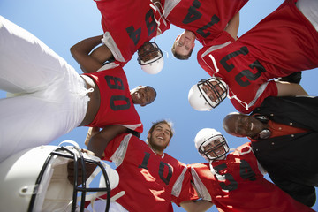 Low angle view of rugby players with coach forming huddle against clear sky