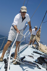Sailors working ropes on deck of a yacht against clear blue sky and sea