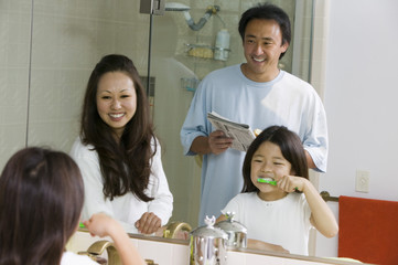 Mirror reflection of Family in Bathroom Getting Ready for Day daughter brushing teeth