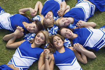 Group of happy young cheerleaders lying on field forming a circle