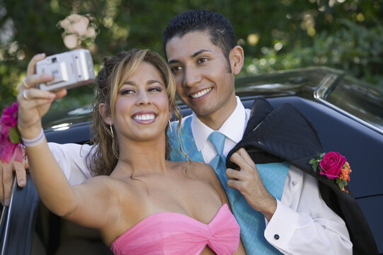 Well-dressed teenage couple taking picture outside car