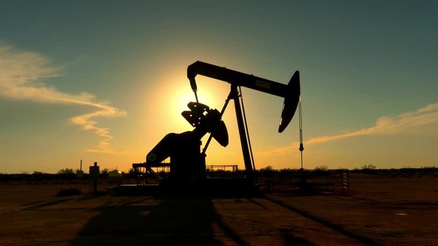 Industrial jack pump platform pumping crude oil over sunset sun
